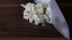 Finely chopped garlic sits on a dark wooden cutting board