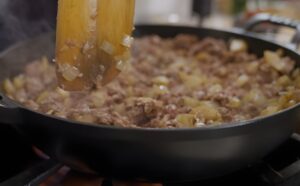 Ground venison and onions are being stirred in a skillet