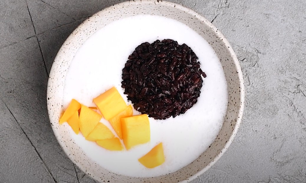 A bowl of black glutinous rice topped with creamy coconut milk and fresh mango slices