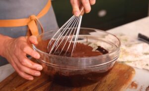 A whisk works through rich, dark chocolate mixture in a glass bowl