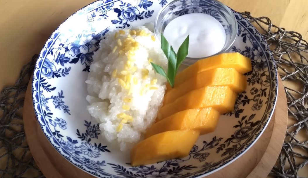 Sweet sticky rice, topped with toasted coconut flakes, served alongside fresh mango slices